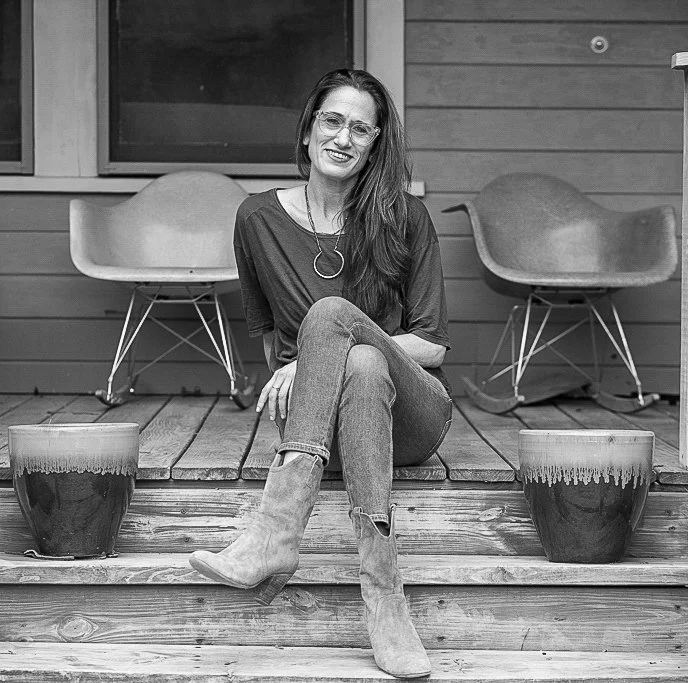 Portrait of Tobin Levy seated on her studio steps beside two ceramic vessels